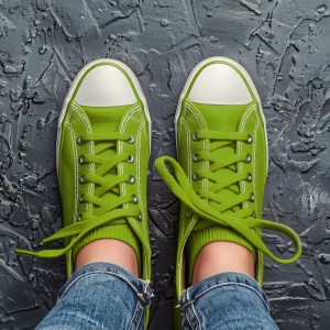 Feet in green sneakers wearing jeans standing on a black surface.
